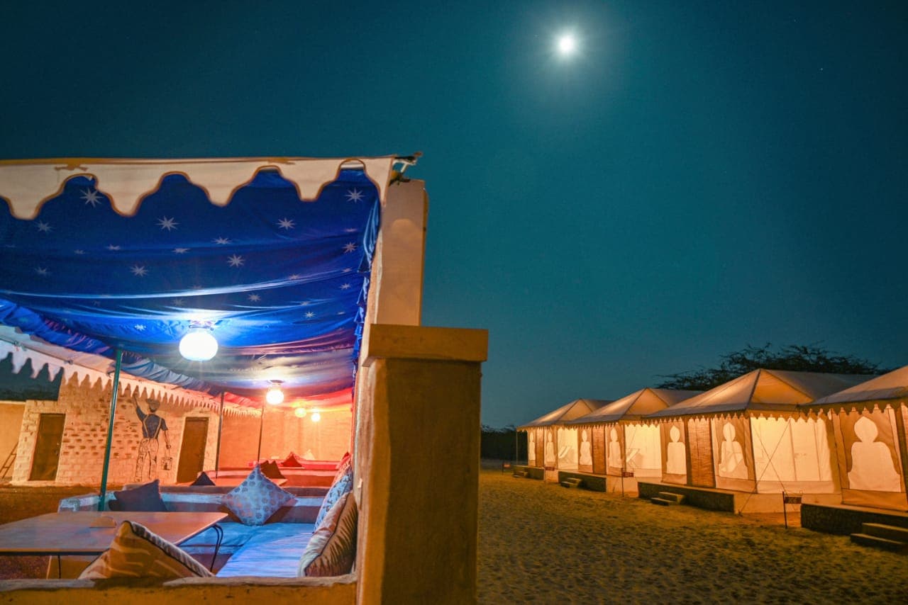 Moonlit outdoor lounge at Explore Overnight Desert Camp Jaisalmer — musicians perform against a backdrop of Swiss tents glowing in the distance