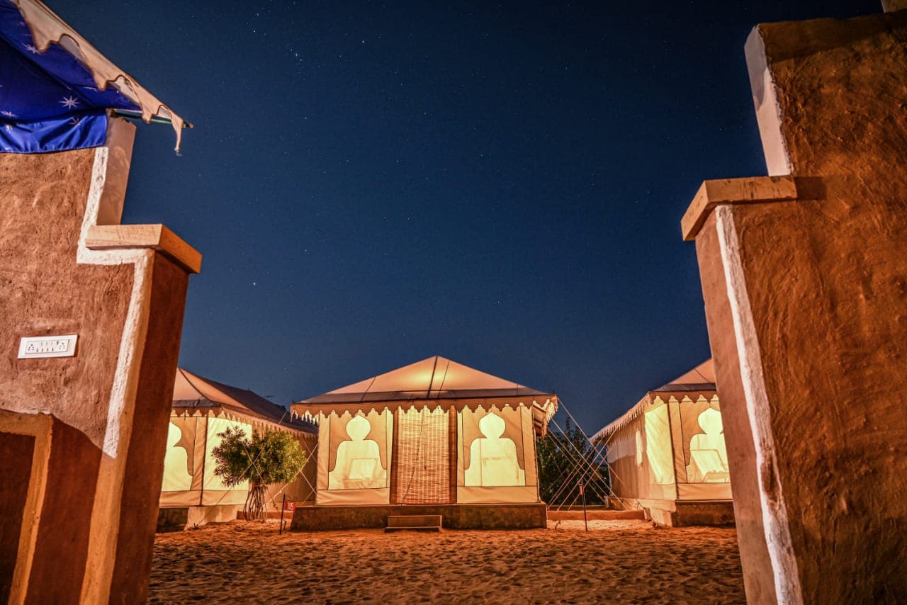 Glowing Swiss tent seen through the camp gateway under a starry sky