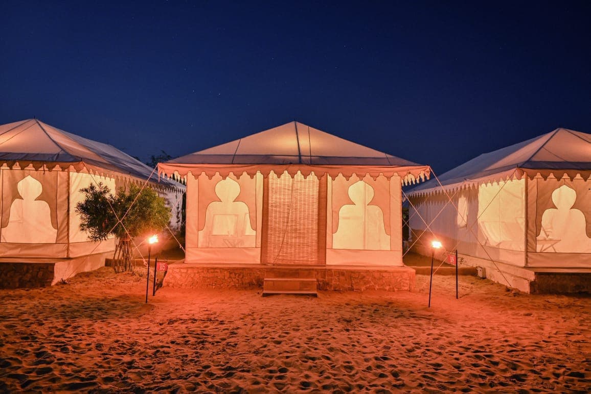 Explore Overnight Desert Camp Jaisalmer Swiss tents glowing warmly in the night sand dunes