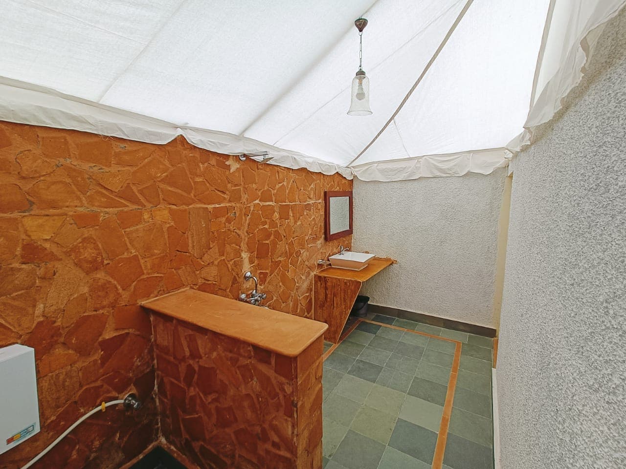 Tent-attached bathroom with Jaisalmer sandstone walls, wall-mounted geyser and sink — actual property photograph